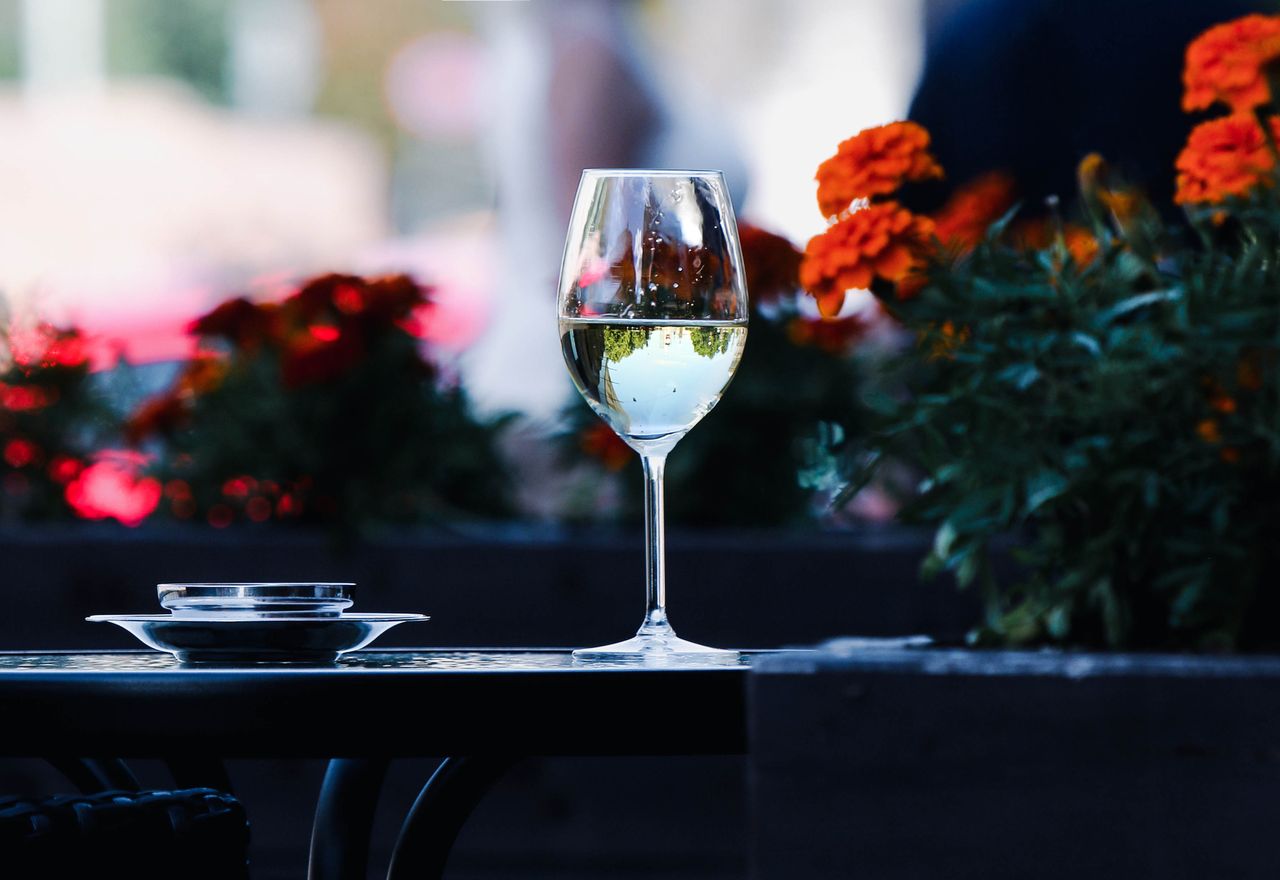 A wine glass on a table surrounded by colorful flowers, capturing a serene outdoor cafe scene.